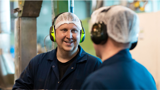 Two men wearing ear defenders in a factory.