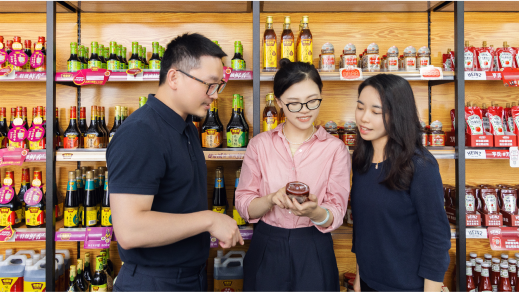 Three people standing in front of a wall with shelves of different sauces and smiling