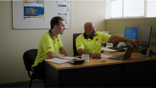 Two men in yellow shirts sitting at a desk.