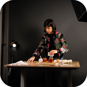 A woman preparing food and bottles of sauces in front of a camera and a set of lights.