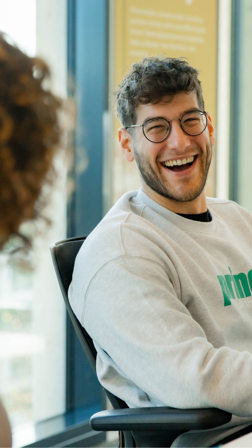 A man laughing at a table with a coworker in an office.