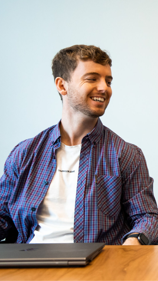A man smiling whilst sitting at a table with a laptop in front of him