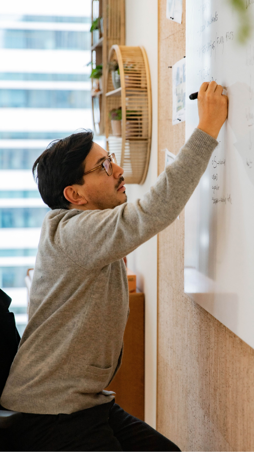 A man sitting down and writing on a whiteboard in an office.