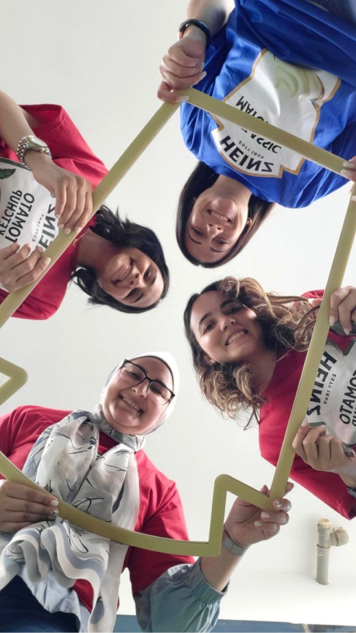 a group of 4 woman looking through a Heinz shaped cutout