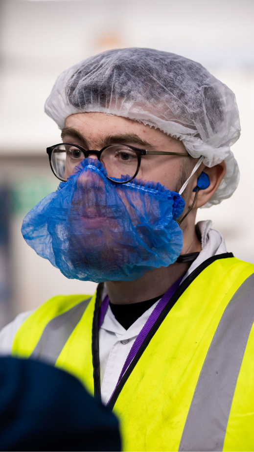 A man wearing protective gear and a high-vis jacket in a factory.