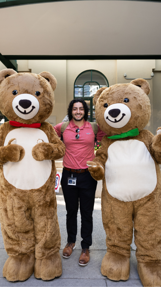 a man standing in between 2 teddy bear mascots