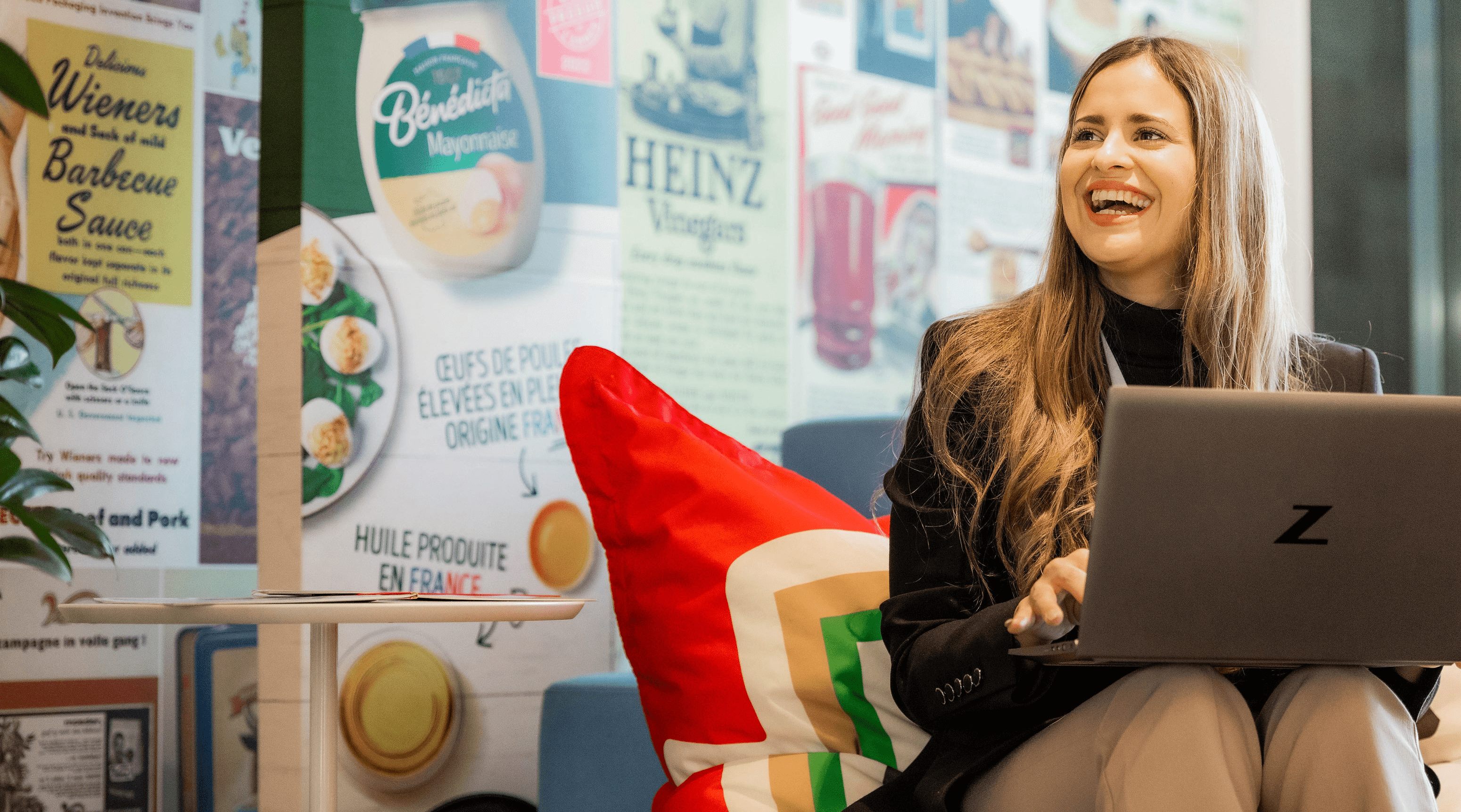 Woman sitting on a colorful couch, smiling, with a laptop on her lap.