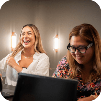 Two women smiling and laughing at their laptops